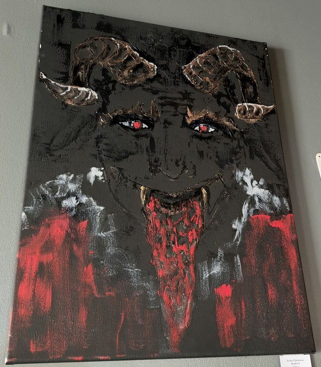 Painting on canvas of a black Krampus face with curled bronze horns, glowing red eyes, fangs and a long red tongue, over streaks of red, white and black