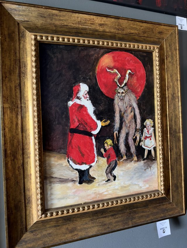 Painting of Santa Claus in his red suit facing a shaggy, antlered Krampus in chains under a red moon, with two small children between them on snowy ground, in a wide gold frame