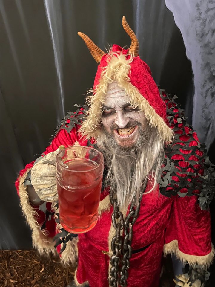 A costumed Krampus character in a red cloak holding a cocktail at Krush Brau Park